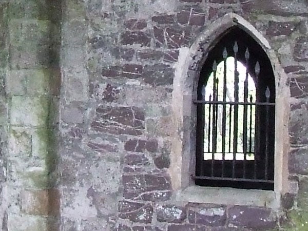 Gothic stone arch window with iron bars in an ancient wall.