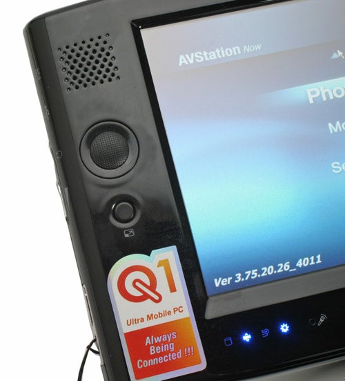 Close-up view of the Samsung Q1 Ultra Mobile PC displaying the AVStation Now screen with speakers visible and status indicator lights. A sticker on the device reads 