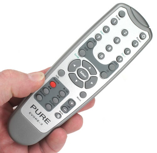 Hand holding a Pure Evoke-3 digital radio remote control with multiple buttons and a silver finish.