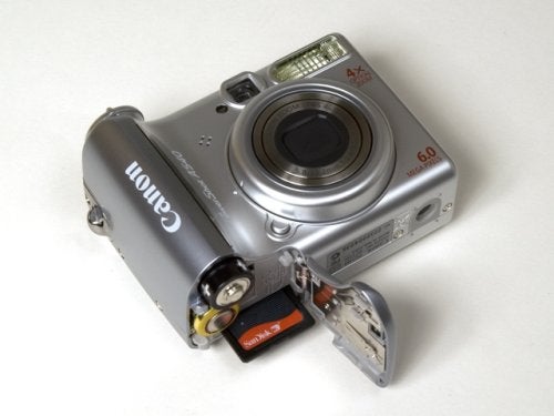 Canon PowerShot A540 digital camera with the battery compartment open showing two AA batteries and an SD card inserted.