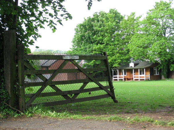Image of a wooden gate leading to a grassy area with trees and a house with a red brick facade and white porch in the background, possibly taken with a Canon PowerShot A540 camera to demonstrate image quality.
