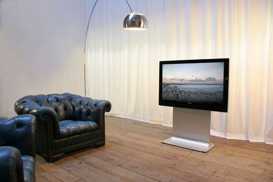 Pioneer PDP-436SXE 43-inch plasma TV on a stand displaying a landscape image in a modern living room with a blue leather couch and a metallic floor lamp.
