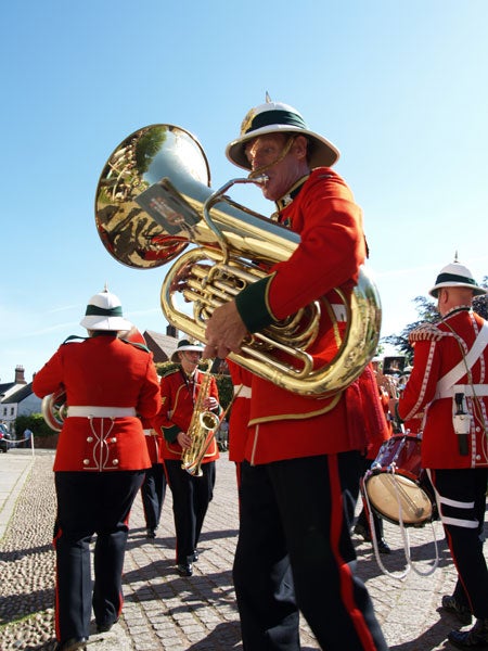 A marching band with members dressed in red uniforms and traditional hats, featuring one person prominently playing a shiny tuba.