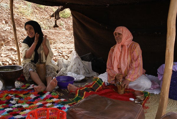 Two women sitting and smiling inside a tent.Close-up of colorful woven fabric texture.