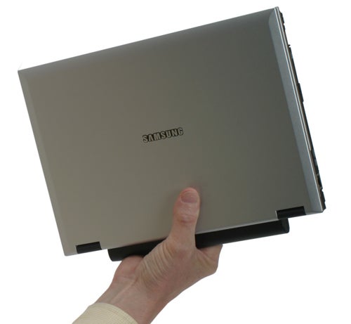 Person holding a closed Samsung Q35 ultra-portable notebook by one corner to demonstrate its lightweight and compact design.
