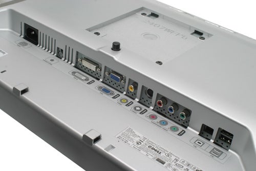 Close-up view of the Dell Ultrasharp 2407WFP 24-inch widescreen monitor's rear input and output ports, including USB, DVI, VGA, S-Video, composite, and component connections. The image also shows the monitor's stand mount and ventilation grilles on a silver background.