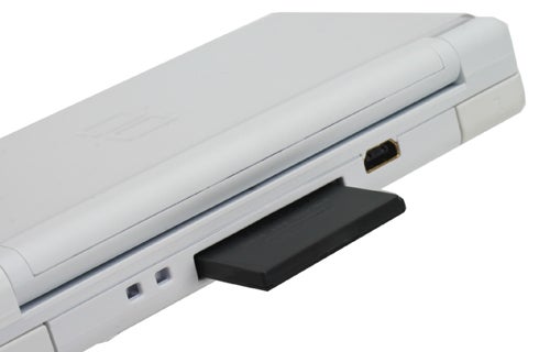 Close-up of a white Nintendo DS Lite handheld console focused on the side view showing the Game Boy Advance cartridge slot and stylus holder.