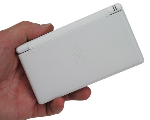 A person holding a white Nintendo DS Lite handheld console in a closed position, showcasing the compact and sleek design of the exterior.