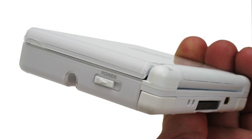White Nintendo DS Lite handheld console held in a person's hand against a white background, side view showing the volume control and GBA slot.