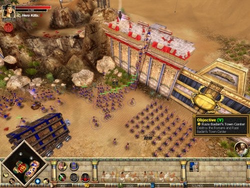 Screenshot from the video game Rise and Fall: Civilizations at War showing an overhead view of a battle scene with troops in formation outside a walled city fortress on sandy terrain. The user interface displays various game controls, a mini-map, and an objective to rescue Batis's Town Center.