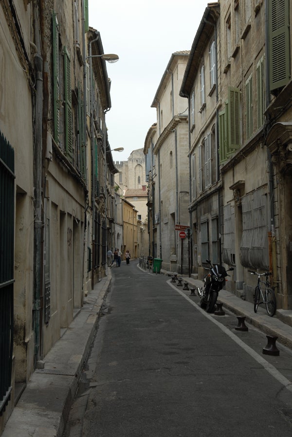 Narrow European street with historic buildings, people walking in the distance, and a motorbike parked on the sidewalk, captured with a Nikon D200 Digital SLR camera.Photograph captured with Nikon D200 showing a narrow European street flanked by old buildings with details visible even in varying light conditions.