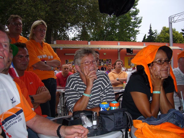 The image provided does not appear to be related to the Panasonic Lumix DMC-FX9. It is a photo of a group of people sitting and standing at an outdoor event, some of whom are wearing orange and appear to be fans of a sports team or participants at a themed event.