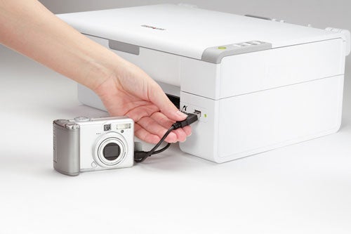 A hand plugging in a USB cable connected to a digital camera into the side of a Lexmark X2470 printer.
