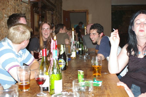 Group of people socializing at a long table with drinks and bottles, capturing casual indoor gathering atmosphere.
