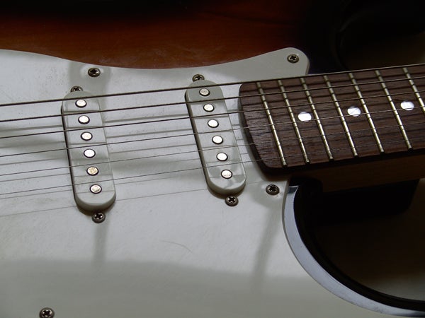 Close-up of a white electric guitar focusing on the pickups and a section of the fretboard with strings.