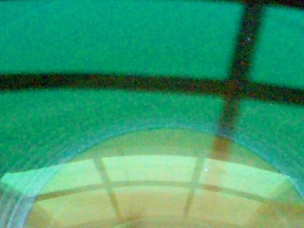 The image is low-resolution and blurry, showing what appears to be a green overhead structure with a partial view of a round, yellow-toned object at the bottom. The quality of the image suggests it might be an example of a photo taken with a Casio Exilim EX-Z1000 Compact Digital Camera under poor lighting conditions or handling, resulting in a lack of clear detail and sharpness.