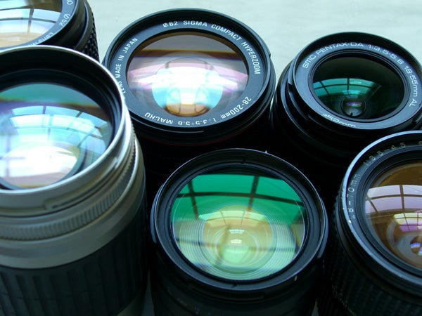A variety of camera lenses arranged in a circle, showcasing different sizes and brands, with reflections on the glass elements.