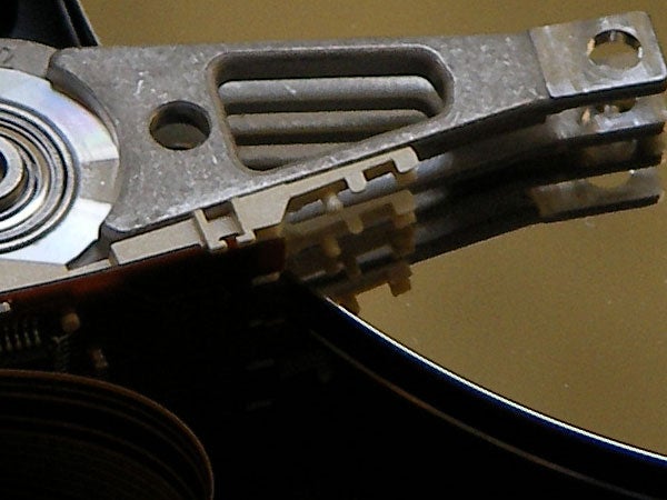 Close-up of a hard drive actuator arm and read/write head over a platter, descriptive of technology components similar to what might be found in electronic devices such as a Sanyo Xacti VPC-HD1 camcorder.