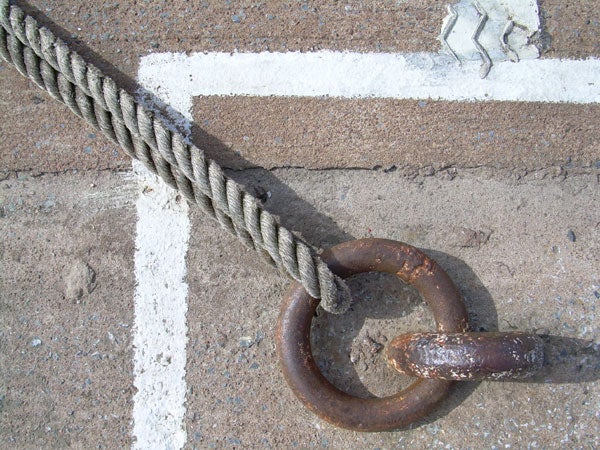 Close-up image of a rusty metal ring attached to a concrete surface with a thick, twisted rope passing through it, taken on a sunny day, showcasing the detail and texture that the Nikon Coolpix L4 camera is capable of capturing.