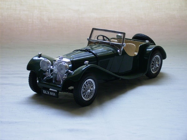 Vintage green sports car model on a beige surface with a spotlight highlighting the vehicle.