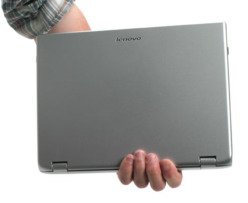 Person holding a closed Lenovo 3000 V100 Ultra Portable Notebook by the corner, showcasing its slim design and matte grey finish.