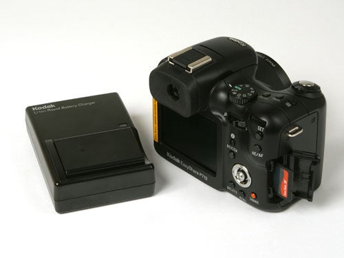 Kodak EasyShare P712 digital camera with a detachable lens hood displayed next to its battery charger on a white background.