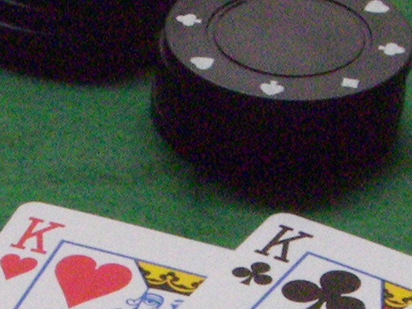 Close-up of a king of hearts and a king of clubs playing cards next to a poker chip on a green surface.