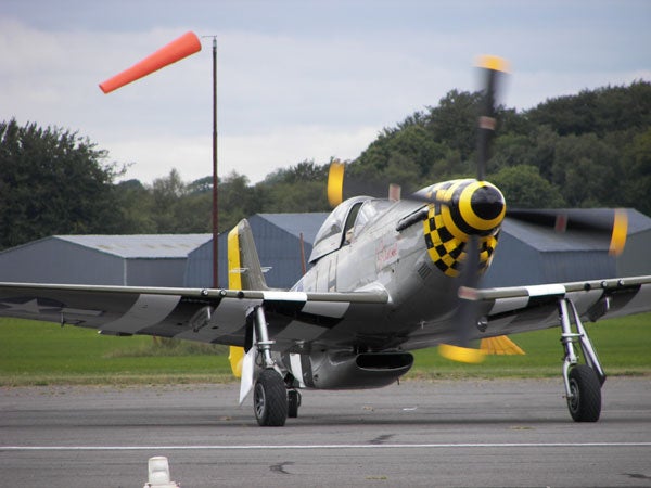 Classic WW2 fighter plane with yellow and black nose parked on the runway with propeller spinning.