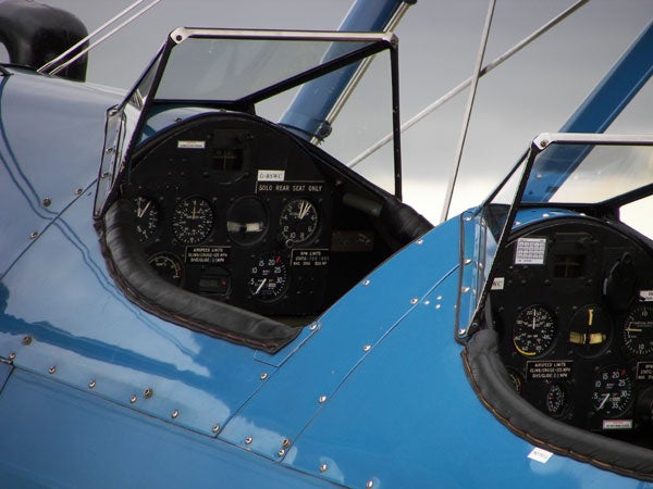 Close-up view of a blue biplane's cockpit showing flight instruments and controls.