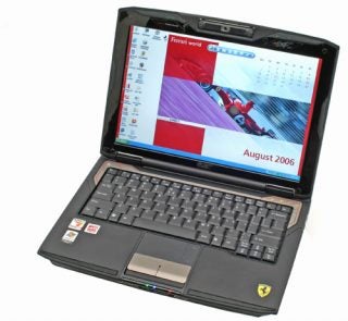 Acer Ferrari 1000 laptop with a black and red color scheme, featuring the Ferrari logo, open on a desk showing a desktop background with a Ferrari car and the calendar for August 2006.