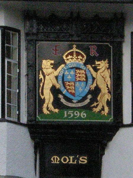 Historical plaque on building facade with heraldic shield and lions.