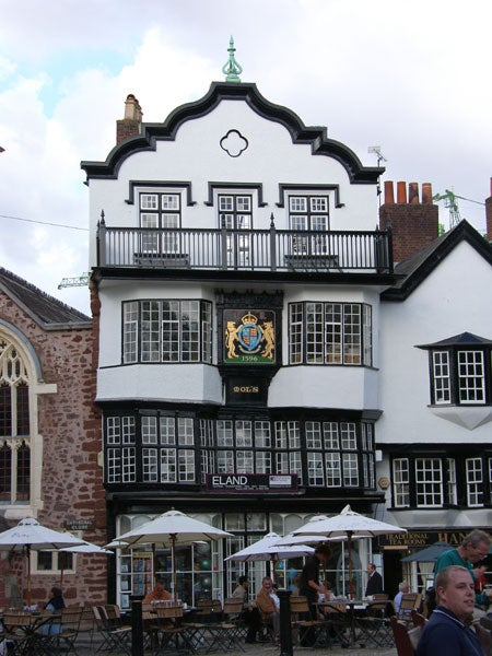 Traditional building with cafe and patrons in the foreground.Royal coat of arms sign with the date 1596 on a building.