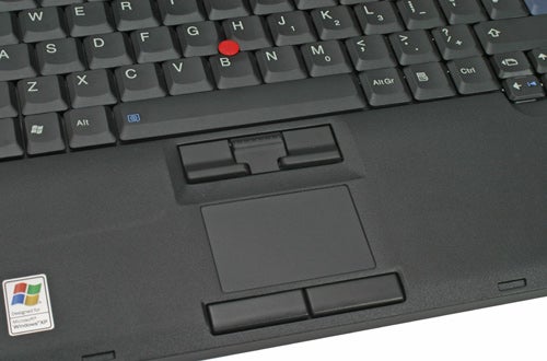 Close-up view of a Lenovo IBM ThinkPad T60p keyboard and trackpad area, highlighting the signature red TrackPoint nub and a Windows sticker on the palm rest.
