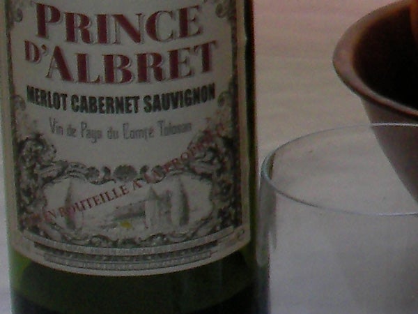 Close-up of a Prince d'Albret Merlot Cabernet Sauvignon wine bottle on a table with a coffee cup slightly out of focus in the background.