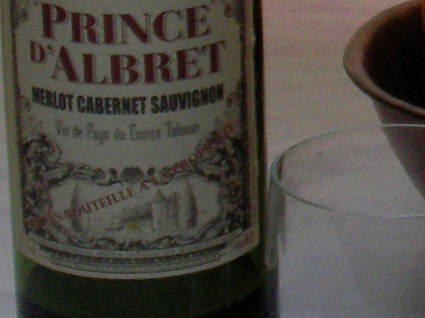 Close-up of a Prince d'Albret Merlot Cabernet Sauvignon wine bottle with a blurred glass in the background.