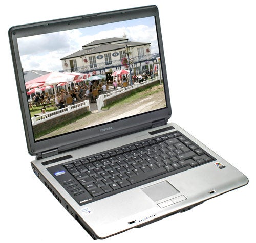 Toshiba Satellite Pro A100 laptop open and powered on displaying a wallpaper of an outdoor event with tents and a historic building in the background.