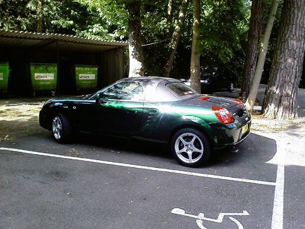 Black sports car parked under the shade of trees next to a designated disabled parking space.