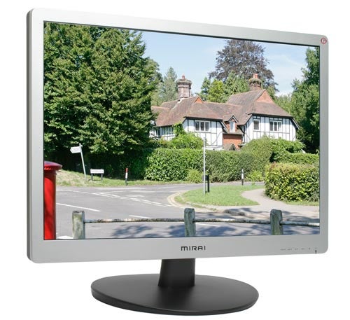 A Mirai DML-522W100 22-inch LCD monitor displaying a vibrant image of a scenic street and houses with a clear sky. The monitor has a silver frame with the Mirai logo at the bottom center and is mounted on a circular black stand.