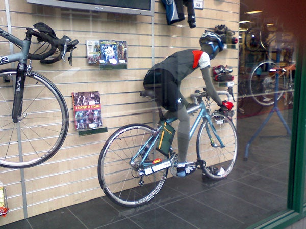 Mannequin dressed in cycling gear riding a bicycle displayed in a bike shop window.