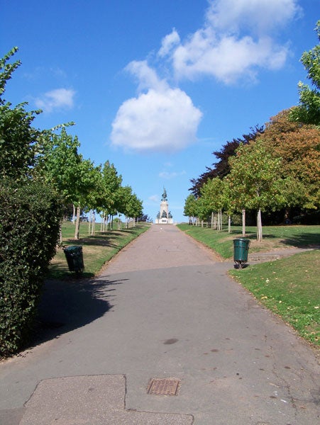 A clear and vibrant image taken with a Kodak EasyShare Z650 camera, showcasing a straight pathway lined with green trees leading up to a statue under a blue sky with few clouds.