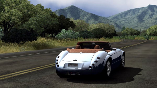 Screenshot from 'Test Drive Unlimited' video game showing a convertible sports car driving on a coastal road with mountains in the distance.
