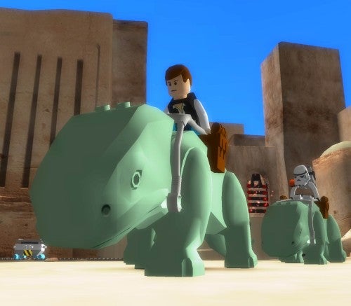 A screenshot from the video game Lego Star Wars II: The Original Trilogy, showing a Lego character resembling Luke Skywalker riding a blocky, Lego-style dewback in a desert setting with a stormtrooper and another character in the background.
