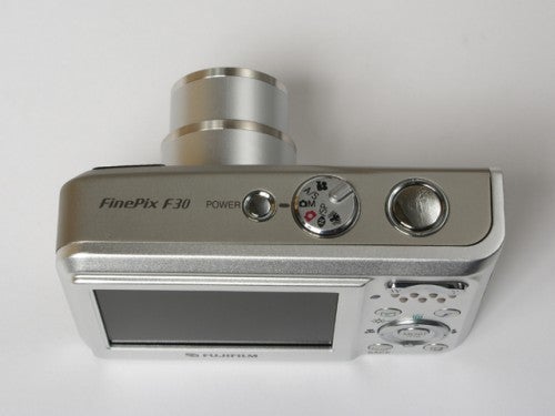 Fujifilm Finepix F30 digital camera displayed on a white background showing the top view with the power button, mode dial, shutter button, and the silver-colored body design.