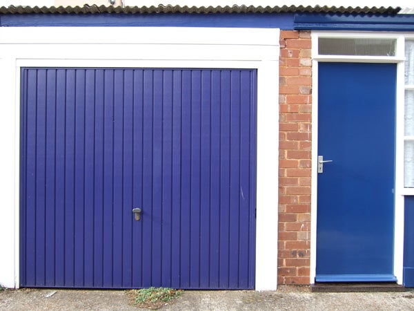 A vivid photograph demonstrating the color reproduction and clarity of the Fujifilm Finepix F30, featuring a blue garage door next to a matching blue house door, with red brick wall and a white window frame, under a gray roof.
