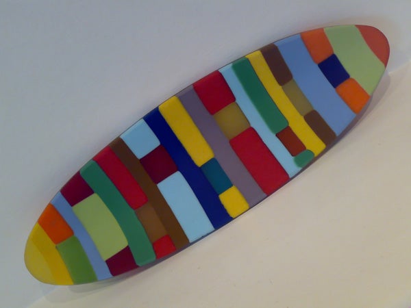 Colorful surfboard-shaped decorative object with multicolored rectangular patterns displayed against a white background.