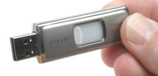 A SanDisk Cruzer Titanium U3 USB flash drive being held between fingers, highlighting its metallic casing and retractable USB connector.