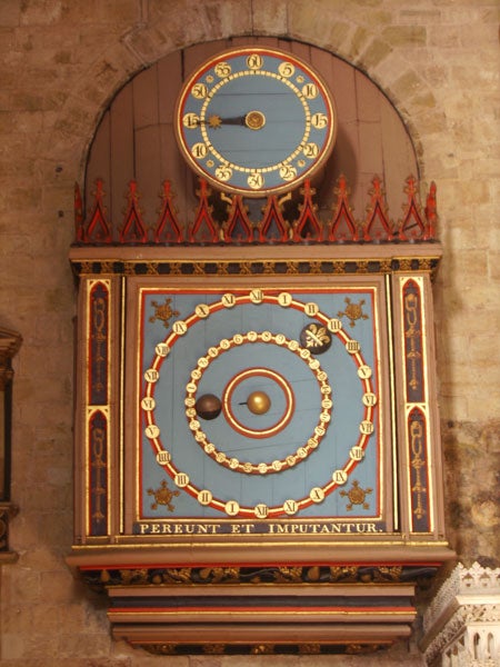 An ornate astronomical clock on an interior wall with gold and blue detailing, Roman numerals, and Latin inscriptions.