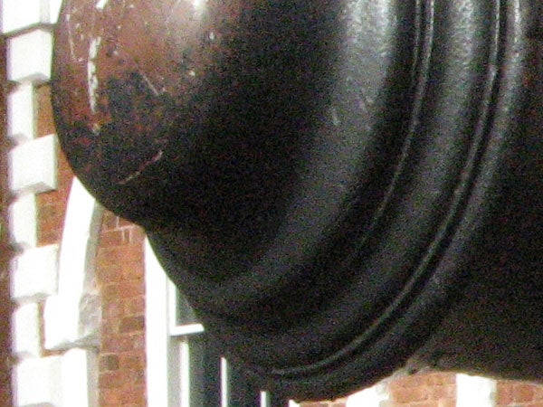 Close-up photograph of a black leather object with a blurred brick wall background.