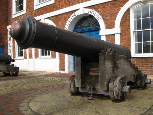 A vintage cannon on display outside a building with a sign reading 'Custom House'.