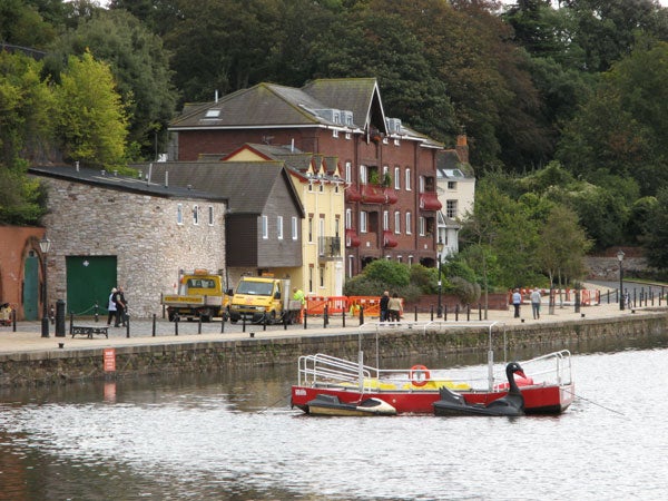 A crisp image taken with the Canon PowerShot A710 IS, showcasing a riverside scene with red and yellow moored boats, various vehicles on the shore, and buildings with foliage in the background.